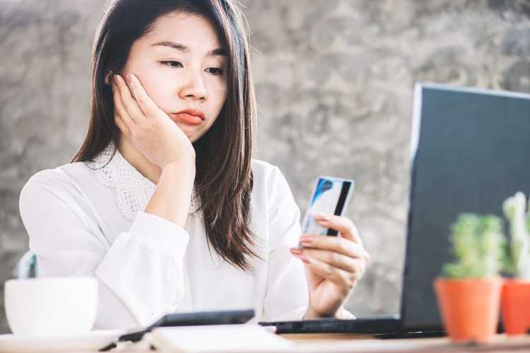 asian woman looking at credit card and bill looking sad