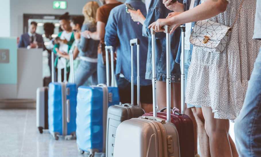 Travelers with luggage using smart phones while waiting in line for boarding at airport