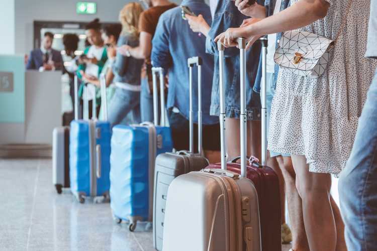 Travelers with luggage using smart phones while waiting in line for boarding at airport